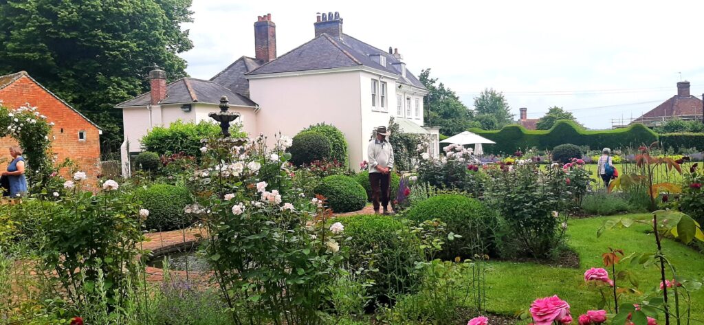 Ringmer u3a garden group walking in gardens, with a pink house in the background