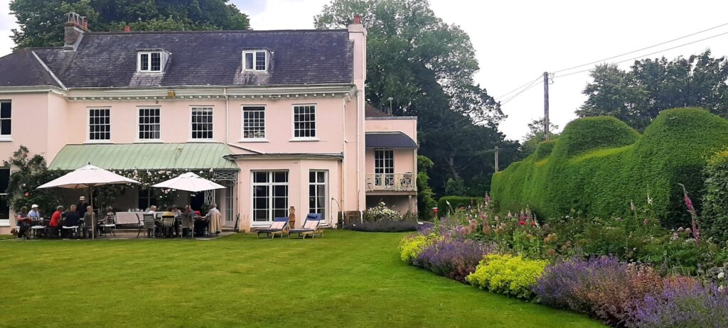 Ringmer u3a garden group walking in gardens, with a pink house in the background