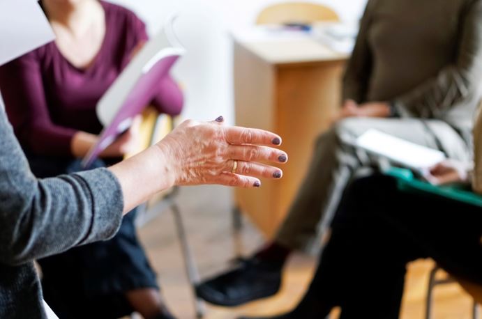 a blurred image of people sitting and a woman's hands giving a talk
